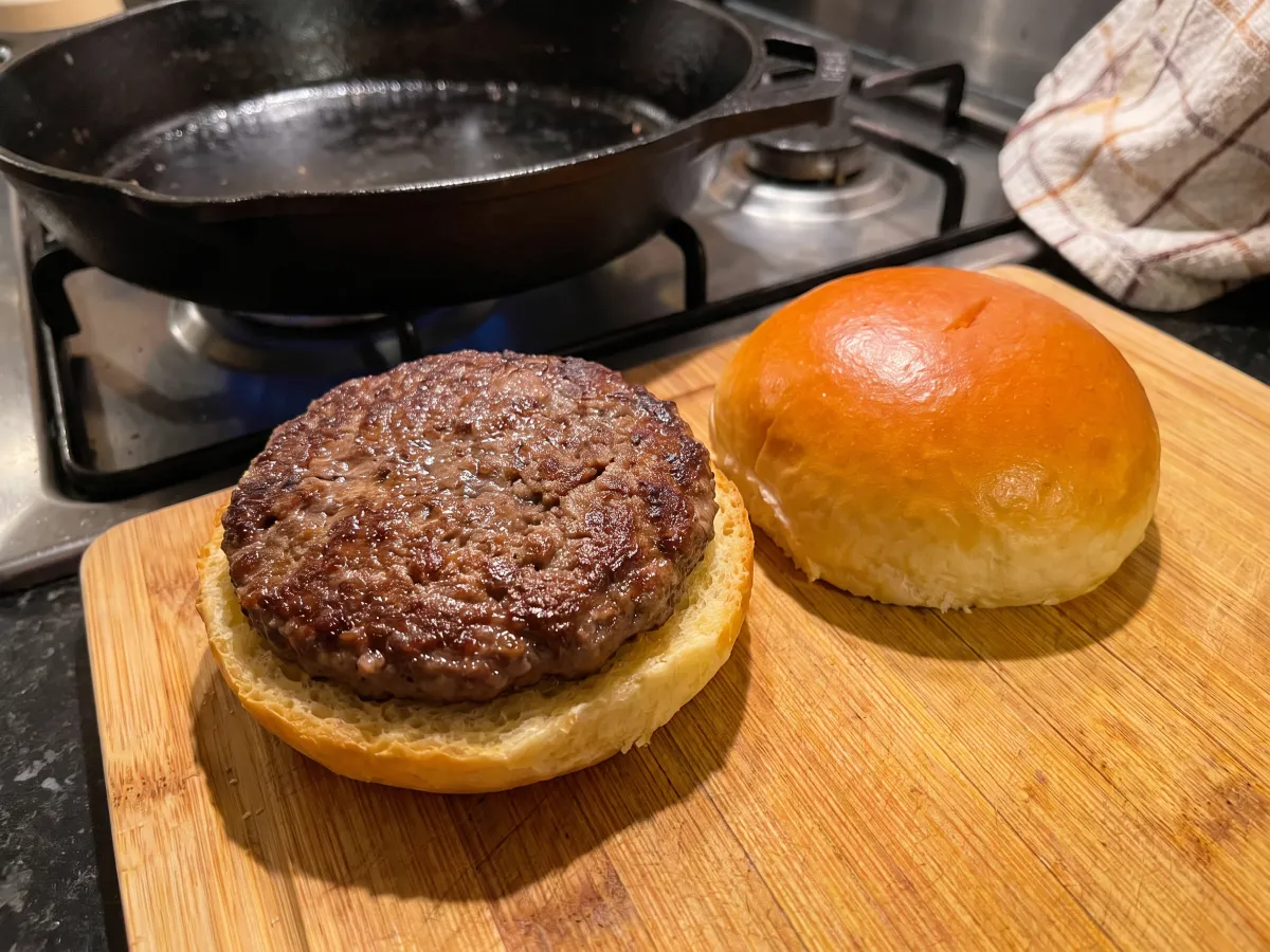 Freshly cooked burger patty on the bottom of a brioche bun of the same diameter