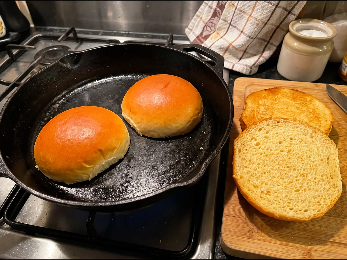 Duas metades de pão brioche a tostar na frigideira e outras duas já tostadas na tábua